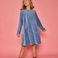 Model can be seen wearing a long sleeve dusty blue velour dress. Dress features button closure at back for a relaxed but secure fit.