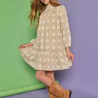 Model can be seen wearing a long sleeve woven dress in a light brown/cream print. Dress features high neck ruffle detail at collar and elastic sleeves for a relaxed fit.