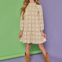 Model can be seen wearing a long sleeve woven dress in a light brown/cream print. Dress features high neck ruffle detail at collar and elastic sleeves for a relaxed fit.