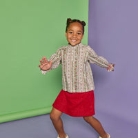 Model can be seen wearing a long sleeve green/red/white woven shirt that features button closures down the front, smocked red detail at sleeve cuffs, and ruffle detail at neckline. Paired back perfectly in our knit sparkly red skort with two pockets on the front to complete the look.