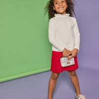 Model can be seen wearing white knit top with high ruffle neckline paired back with a red sparkly fabric knit skort that has pockets on the front.