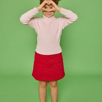 Model can be seen wearing a long sleeve ribbed knit turtleneck in bubblegum pink paired back with a red sparkly knit skort that has two pockets in the front and elastic waistband.