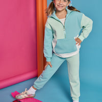Model can be seen wearing a knit color block set in a teal and light green color. Pullover top features a quarter zip zipper and front pocket. Joggers have on pant leg in the aqua and one in the light green color for an elevated look.