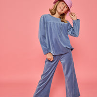 Model can be seen wearing a matching dusty blue velour set. Long sleeve top features button closure at back and pants feature pockets and an elastic waistband for a relaxed but secure fit.
