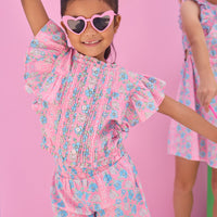 Model can be seen wearing a woven pink and blue floral top that features button closures along the front and big angel sleeve detail to elevate the look. Top pairs back perfectly with the shirred shorts in the same matching print to complete the look.