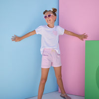 Tween model can be seen wearing pink sparkly seersucker woven shorts that feature an elastic waistband and two pockets in the front. Shorts pair back perfectly with basic white tee with faux heart pocket in the same pink seersucker fabric to complete the look.