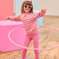 Child in pink sweater and leggings with hula hoop on wooden floor
