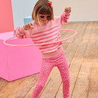 Child in pink striped sweater and floral print pants playing with a hula hoop on a wooden floor.