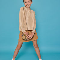 Model can be seen wearing a long sleeve woven top in a tan/cream print. Top features button closure packet down bust and smocking detail at sleeves for an elevated look. Paired back with our brown faux suede skort that has built in shorts and pocket detail at front.