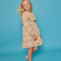Model can be seen wearing long sleeve woven khaki gingham dress. Dress features buttons down the front and a ruffle at the bodice for an elevated look.