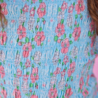 Model can be seen wearing woven pink and aqua floral print top that features elastic smocking throughout the body of the top for a stretchy but secure fit.
