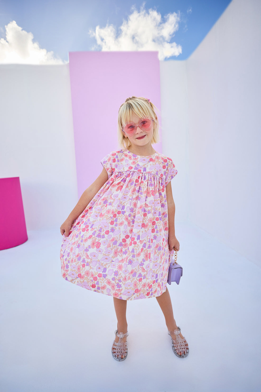 Girls/tween woven dress in a lavender/salmon floral print with matching lavender piping across bust and sleeves. Dress features button closures along back and made of a lightweight material that is lined for a secure but comfy fit.