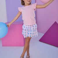Model can be seen wearing two tiered skort in a blue/red/pink pattern that features scallop edges in pink embroidery, built in shorts, and an elastic waistband. Skort pairs back perfectly with the knit light pink top that features an eyelet detail on the angel sleeves to complete the look.