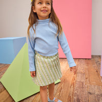 Model can be seen wearing a soft light blue ribbed turtleneck paired back with a beautiful green skort that features a silver metallic and white pattern to elevate the look.