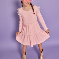 Model can be seen wearing soft knit ribbed pink dress that has sparkle star tulle along two tiers and the same tulle at sleeves for an angel sleeve effect.