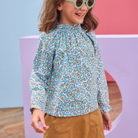 Model can be seen wearing brown/blue/green floral print woven shirt that features a high neck elastic collar which gives it the ruching affect. Top pairs back perfectly with brown faux suede skort to complete the look.