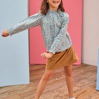 Model can be seen wearing brown/blue/green floral print woven shirt that features a high neck elastic collar which gives it the ruching affect. Top pairs back perfectly with brown faux suede skort to complete the look.