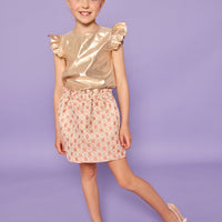 Model can be seen wearing gold metallic lurex top that features angel sleeve detail and button closure at back. Paired back with jacquard skirt with pink and gold metallic details.