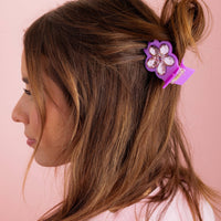 Woman with brown hair with a purple hair clip against a pink background