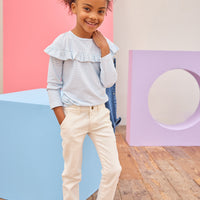 Tween girl seen wearing a pale blue and white stripe ruffle long sleeve t-shirt paired back with ivory denim jeans for an elevated but comfy look.