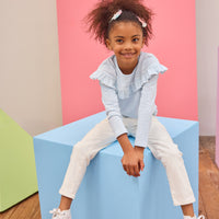 Tween girl seen wearing a pale blue and white stripe ruffle long sleeve t-shirt paired back with ivory denim jeans for an elevated but comfy look.