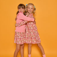 Model on right can be seen wearing long sleeve knit dress in red/yellow/floral print while the model on the left can be seen wearing a long sleeve pink and white stripe knit t-shirt that features ruffles at the sleeves. Paired back with our skort in a red/pink/yellow floral print, that has built in shorts, to complete the look.