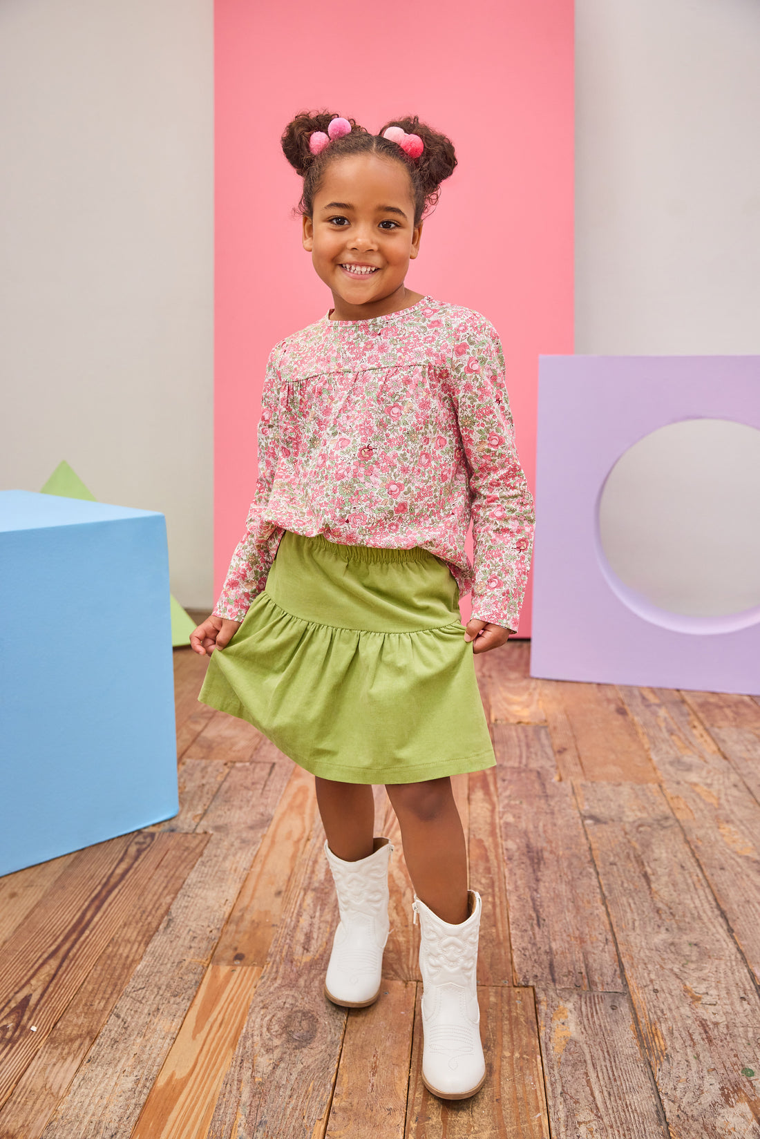 Model can be seen wearing long sleeve woven top in a pink/green floral pattern. Top features a button closure at back and a pleating feature at bust for an elevated look. Top pairs back perfectly with a corduroy skort in the matching green to complete the look.