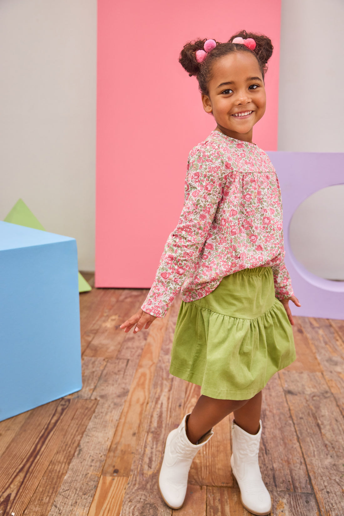 Model can be seen wearing long sleeve woven top in a pink/green floral pattern. Top features a button closure at back and a pleating feature at bust for an elevated look. Top pairs back perfectly with a corduroy skort in the matching green to complete the look.