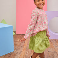 Model can be seen wearing long sleeve woven top in a pink/green floral pattern. Top features a button closure at back and a pleating feature at bust for an elevated look. Top pairs back perfectly with a corduroy skort in the matching green to complete the look.