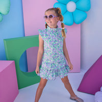 Model can be seen wearing a woven aqua/purple floral top that features angel sleeve details, high ruffle neckline, and button closure on back for a comfy but secure fit. Matches back perfectly with the tiered skort in the same floral print to complete the look.