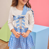 Tween model can be seen wearing a white long sleeve t-shirt paired with a knit blue floral skort with a blue and white stripe sweater tied over the shoulder to complete the look.