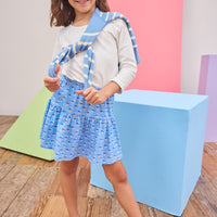 Young girl in a blue and white outfit with sunglasses standing on a wooden floor.