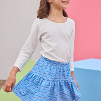 Young girl wearing a white long-sleeve shirt and blue skirt with a pattern against a colorful background