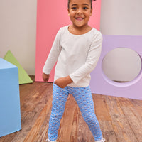 Young girl in a white top and blue patterned pants standing in a room with colorful geometric shapes on the wall.