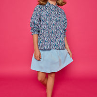 Model can be seen wearing a woven top with a ruffle neckline and button closure along back. The purple/teal/blue floral print pairs back perfectly with our skort in light blue corduroy to complete the look.