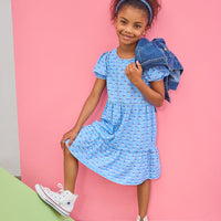 Young girl in a blue dress with a denim jacket against a pink background
