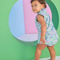 Baby model can be seen wearing a woven bloomer set in an aqua/green/purple floral print. Top of set features button closure at back and bottom features elastic waistband for easy put on/pull off access.