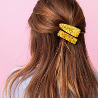 Long brown hair with a yellow hair clip against a pink background