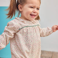 Baby girl can be seen wearing a woven bubble in a gorgeous red and green color floral that features a ruffle neckline and snap closure for easy put on/pull off access.