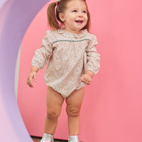 Baby girl can be seen wearing a woven bubble in a gorgeous red and green color floral that features a ruffle neckline and snap closure for easy put on/pull off access.