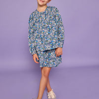 Model can be seen wearing a long sleeve woven dress in a blue/purple/white floral print. Top features ruching across the bust and elastic at the sleeves.