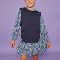 Model can be seen wearing a long sleeve woven dress in a blue/purple/white floral print. Top features ruching across the bust and elastic at the sleeves. Can also be paired underneath a navy sweater vest for a more elevated look.