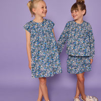 Models can be seen wearing a floral print in blue/purple/and green. Print comes in a short sleeve woven dress and in a long sleeve woven top and skirt for options for little girl.