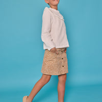 Model can be seen wearing a white eyelet top in a woven embroidered fabric that has buttons down the front, and a ruffle detail along the bust. Paired back with our brown corduroy skirt that has faux pockets and white flowers to complete the look.