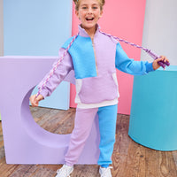 Model can be seen wearing a matching color block set in purple/aqua/and white. Pullover features a gold quarter zip zipper detail and large front pocket for a relaxed but secure fit. Pullover matches back perfectly to the joggers, and continues with the color block with a purple pant leg and an aqua pant leg.