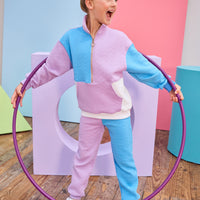 Model can be seen wearing a matching color block set in purple/aqua/and white. Pullover features a gold quarter zip zipper detail and large front pocket for a relaxed but secure fit. Pullover matches back perfectly to the joggers, and continues with the color block with a purple pant leg and an aqua pant leg.