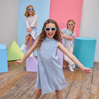 Children posing in front of colorful geometric shapes on a wooden floor in matching outfits.