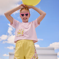 Model can be seen wearing pink and white stripe knit boxy tee that features a floral patch pocket that matches back perfectly with the pink/yellow floral trim on the track shorts to complete the look.