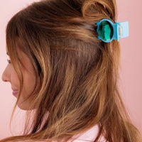 Woman with a blue hair clip in her brown hair against a pink background