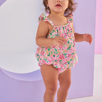 Baby girl woven bubble in a hot pink/yellow/green floral pattern. Bubble features button closures along back and stride and strappy angel sleeves for an elevated look.